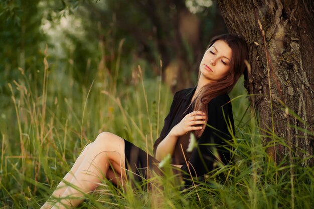 Sincero omitiendo despreocupada mujer adorable en campo cerca del árbol al atardecer de verano.