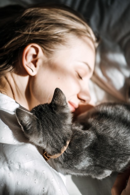 El sincero retrato de una joven descansa con una mascota gatita en la cama en casa un día soleado