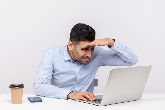 Síndrome da visão computacional. Empregado de escritório masculino trabalhando no laptop e olhando cuidadosamente para a tela, mantendo a mão sobre os olhos focando na tela, tendo problemas de visão. tiro de estúdio interno isolado