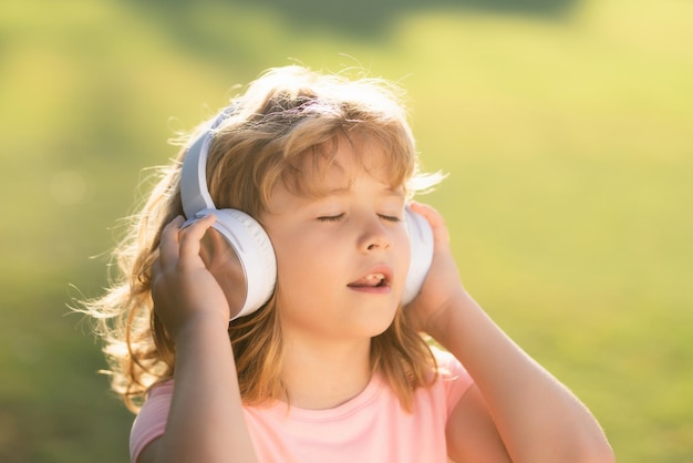 Singende Kinder, stilvoller Teenager, der Musik in Kopfhörern hört und gegen grünes Gras summt