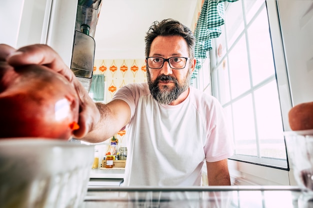 Single einsamer Mann zu Hause im Erwachsenenalter, der in einen leeren Kühlschrank schaut, um zu wählen, was er essen soll