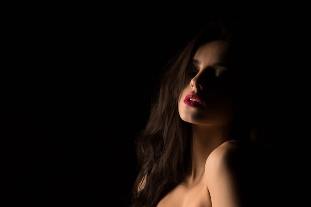 Sinnliche brünette junge Frau mit nackten Schultern posiert im dunklen Studio