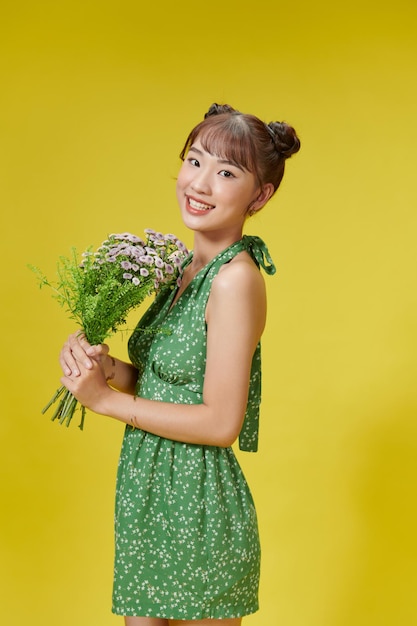 Sinnliche Frau hält Blumen fest in der Hand und genießt sommerliche Posen vor gelbem Hintergrund