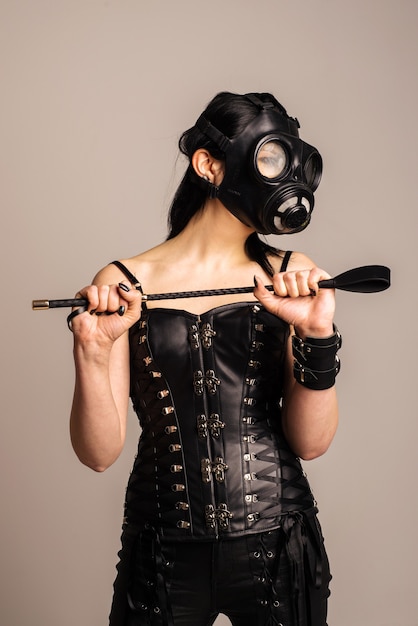 Sinnliche Frau im schwarzen Lederkorsett mit Gasmaske und Reitgerte in der Hand