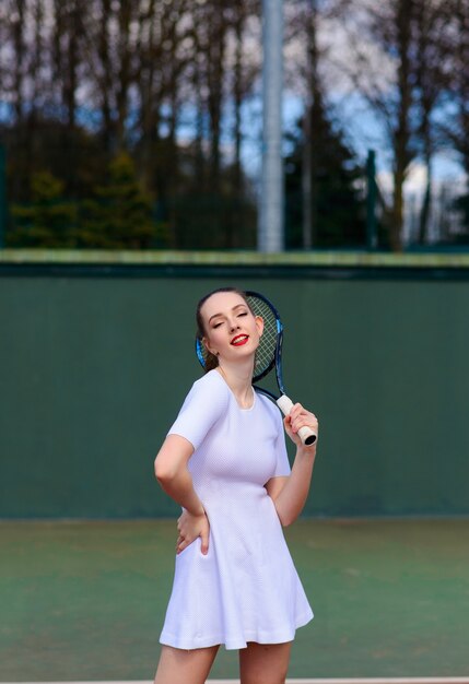 Sinnliche Frau mit Tennisschläger am Netz auf Rasen. Aktivität, Energie, Kraft. Sporttraining. Wellness Körperpflege Gesundheit