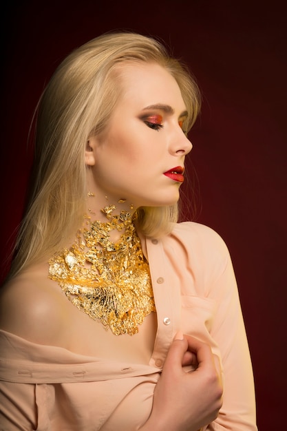 Sinnliches Model mit langen blonden Haaren und goldenen Folienmustern auf der Haut, das auf schwarzem Hintergrund posiert