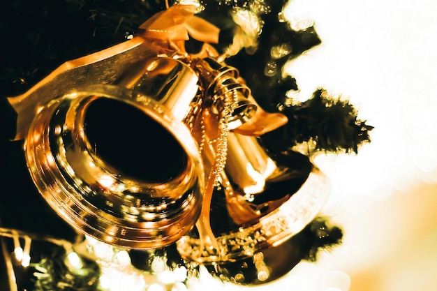 Foto sinos dourados com um laço vermelho na árvore de natal borrado fundo bokeh brilhante
