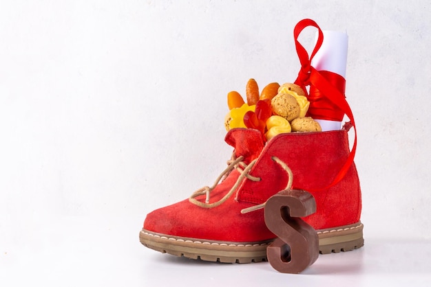 Sinterklaas Sankt-Nikolaus-Tag-Hintergrund Roter Schuh des kleinen Kindes mit Karotten und Süßigkeiten Trooigoed Pepernoten-Süßigkeit Niederländische Weihnachtsgrußkarte