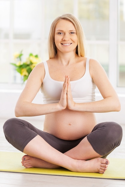 Sintiendo armonía por dentro. Hermosa mujer embarazada meditando mientras está sentado en posición de loto