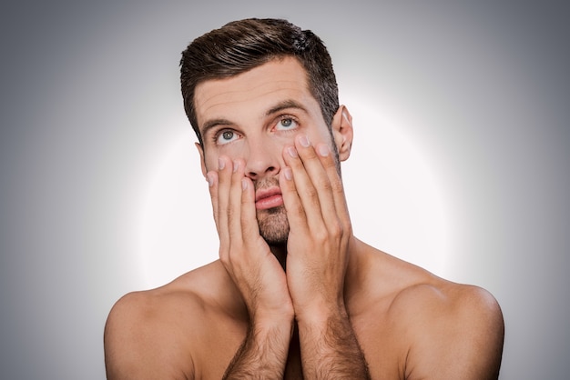 Sintiéndome tan aburrido. Retrato de hombre sin camisa joven aburrido que cubre la boca con la mano y bosteza mientras está de pie contra el fondo gris