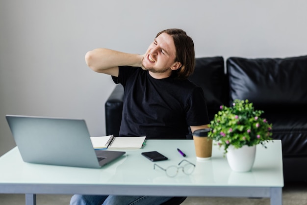 Sintiéndose agotado Frustrado joven apuesto que parece exhausto mientras se sienta en su lugar de trabajo y lleva sus gafas en la mano