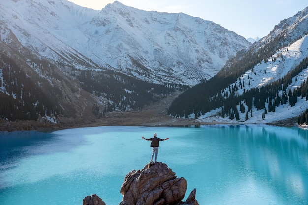 Sintiéndose en la cima del mundo hombre de pie sobre una roca sobre un lago de montaña