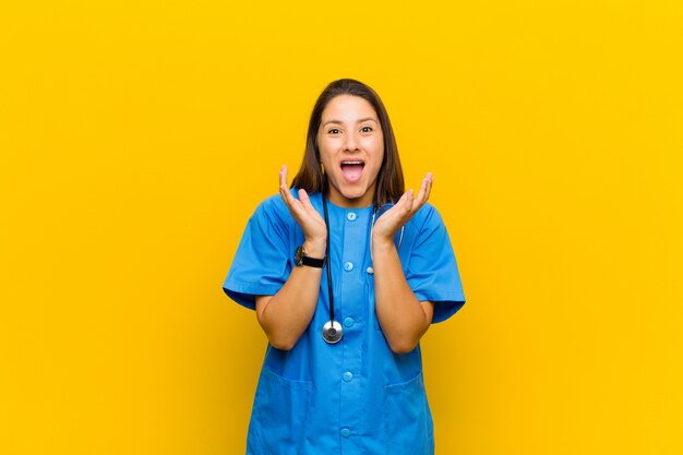 Foto sintiéndose conmocionado y emocionado, riendo, asombrado y feliz debido a una sorpresa inesperada aislada contra la pared amarilla