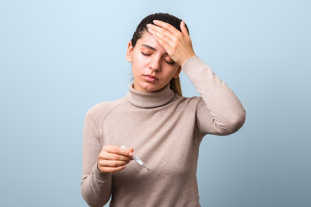 Síntomas de coronavirus. Mujer con fiebre y dolor de cabeza con termómetro buscando desesperado contra el fondo azul.