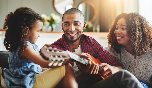 Sintonizado con el tiempo en familia Foto de una niña adorable y sus padres tocando una guitarra juntos en el sofá de casa