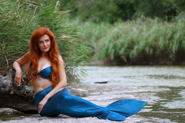 una sirena con un traje azul con el pelo largo y rojo en el río
