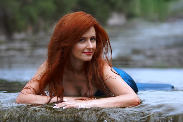 una sirena con un traje azul con el pelo largo y rojo en el río