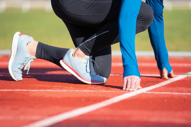 Sirva al atleta en la línea de salida de una pista de atletismo en el estadio, cierre para arriba.