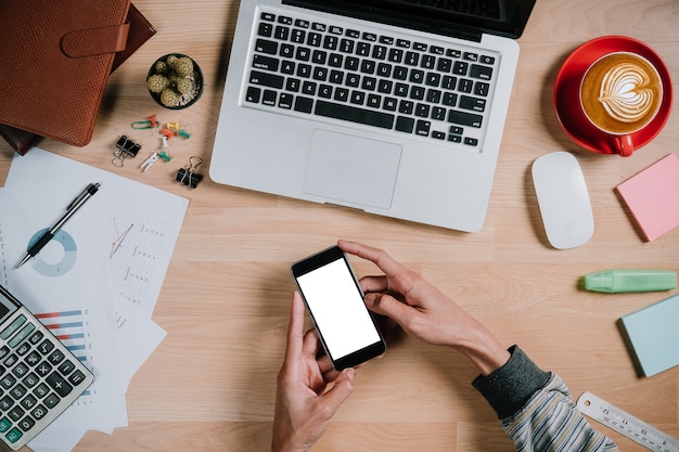 Sirva las manos que sostienen la pantalla en blanco un smartphone en el escritorio de trabajo.