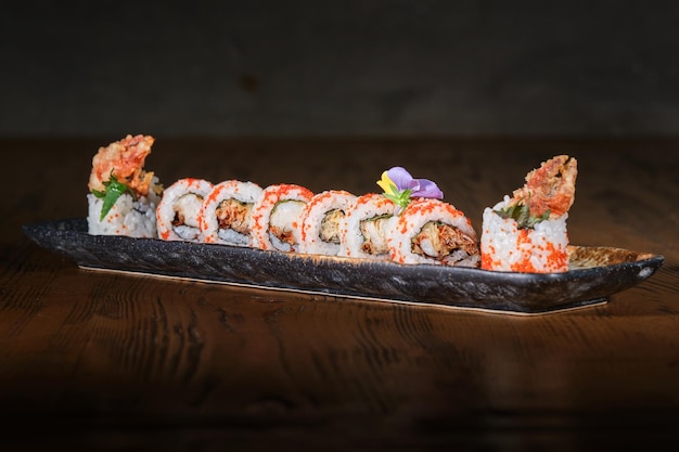 Se sirve un juego de sushi uramaki japonés con huevas de pescado tobiko rojo y garras de cangrejo fritas en tempura sobre una mesa de madera