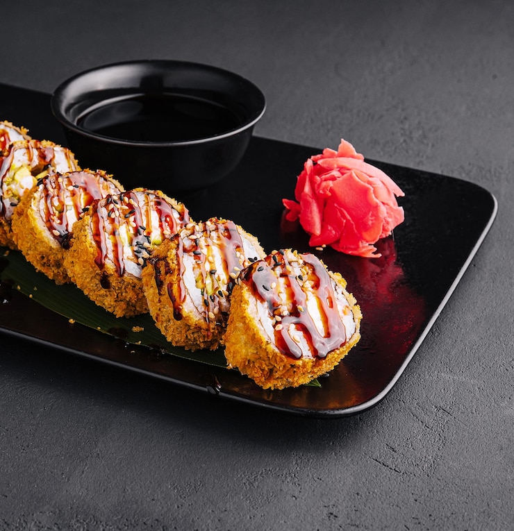 Se sirve sushi tibio con jengibre y wasabi en un plato de piedra negra