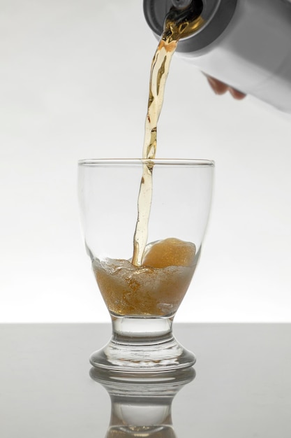 Sirviendo una lata de cerveza en un vaso de cristal con un fondo blanco.