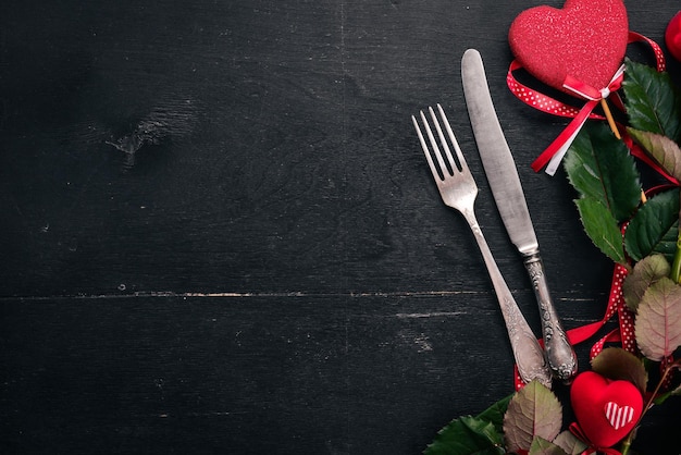 Sirviendo la mesa para celebrar el día de los enamorados. Cubiertos, platos, rosas. Sobre un fondo de madera. Vista superior. Espacio libre para su texto.