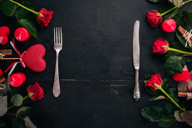 Sirviendo la mesa para celebrar el día de los enamorados. Cubiertos, platos, rosas. Sobre un fondo de madera. Vista superior. Espacio libre para su texto.