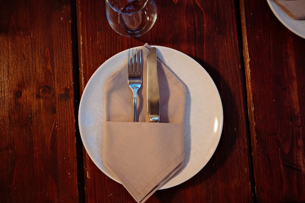 Sirviendo la mesa. tenedor y cuchillo en una servilleta en un plato. cubiertos para una cena festiva. Luz baja.