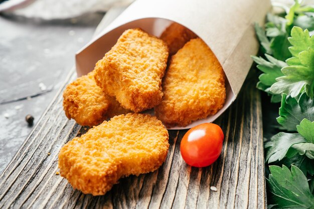 Sirviendo de nuggets de pollo en bolsa de papel artesanal con semillas de sésamo, tomates cherry, perejil sobre superficie de madera