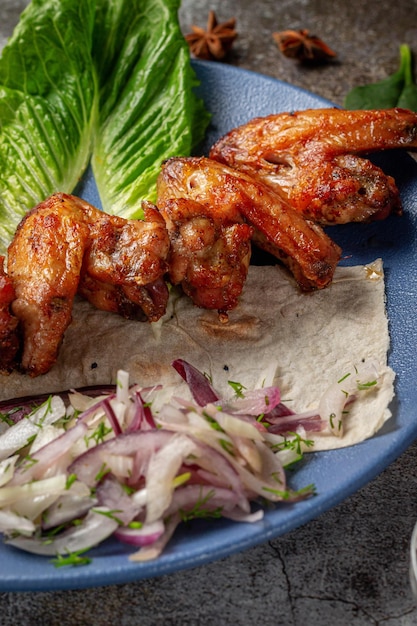 Sirviendo un plato de la carta del restaurante. Alitas de pollo, nuggets a la parrilla con zanahorias ralladas y hierbas en un plato contra una mesa de piedra gris, delicioso kebab