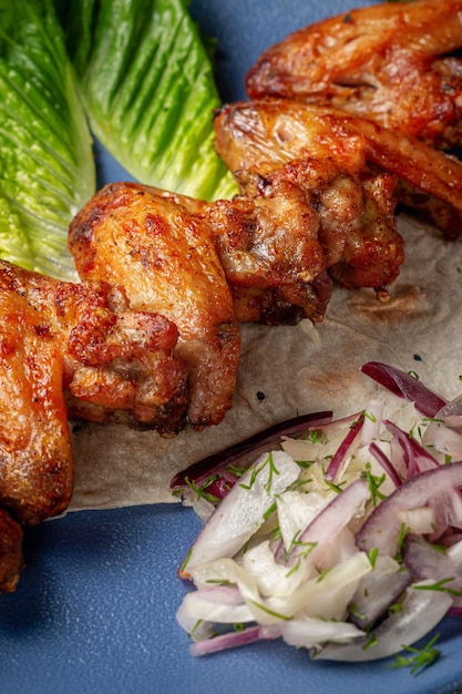 Sirviendo un plato de la carta del restaurante. Alitas de pollo, nuggets a la parrilla con zanahorias ralladas y hierbas en un plato contra una mesa de piedra gris, delicioso kebab