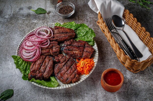 Sirviendo un plato de la carta del restaurante. Carne de res y cerdo a la parrilla con zanahorias ralladas y hierbas en un plato contra una mesa de piedra gris, delicioso kebab