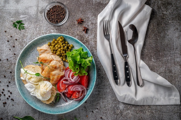 Sirviendo un plato de la carta del restaurante. Pechuga de pollo con verduras y verduras, tomates, cebollas, tortillas y guisantes en un plato con el telón de fondo de una mesa de piedra gris