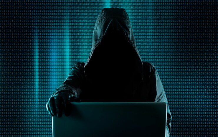 Foto sistema de piratería, ciberdelincuente detrás de una computadora portátil, código binario digital en segundo plano. hacker irrumpe en el sistema