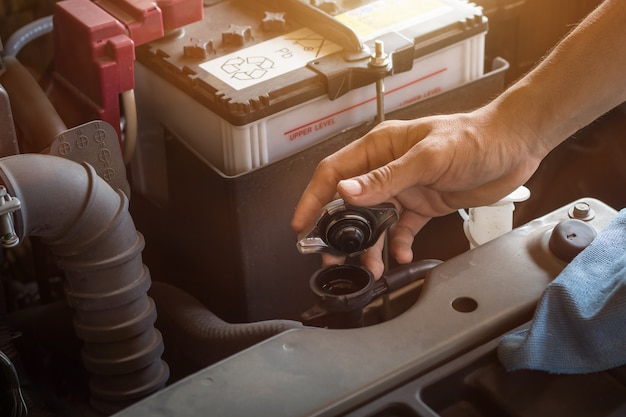 El sistema de verificación de funcionamiento del mecánico de automóviles y el agua de la batería llenan el motor de un automóvil viejo en la estación de servicio, cambian y reparan antes de conducir