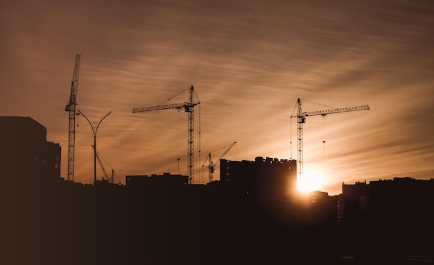 Sitio de construcción con grúas de construcción y casas en construcción con un fondo de puesta de sol.