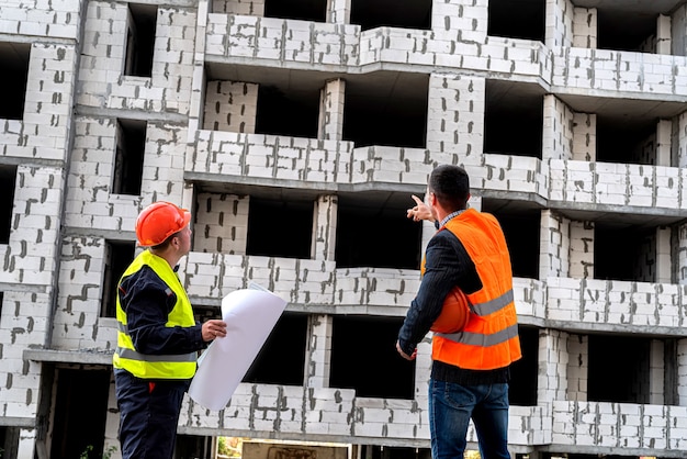 En un sitio de construcción, un trabajador en uniforme le muestra a otro trabajador en uniforme un plano de la casa. Concepto de construcción