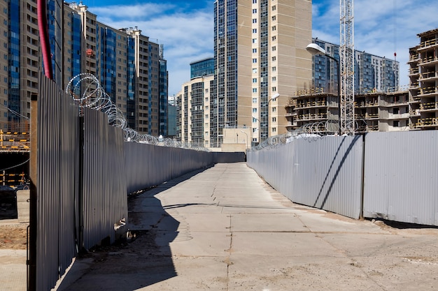 Sitio de construcción con vallas y camino de hormigón con el telón de fondo del complejo residencial de apartamentos en creación. Vista de la zona de peligro industrial. Concepto de rehabilitación de viviendas. Copia espacio