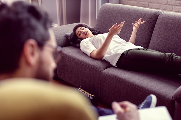 Situación difícil. Bonita mujer guapa mirando al terapeuta mientras comparte sus preocupaciones con él.