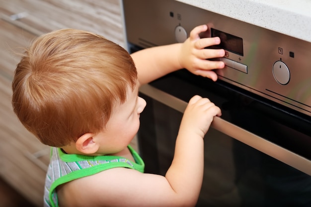 Situación peligrosa en la cocina. Niño jugando con horno eléctrico.