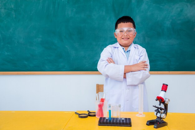 Situación y sonrisa asiáticas jovenes del estudiante en sala de clase de la ciencia