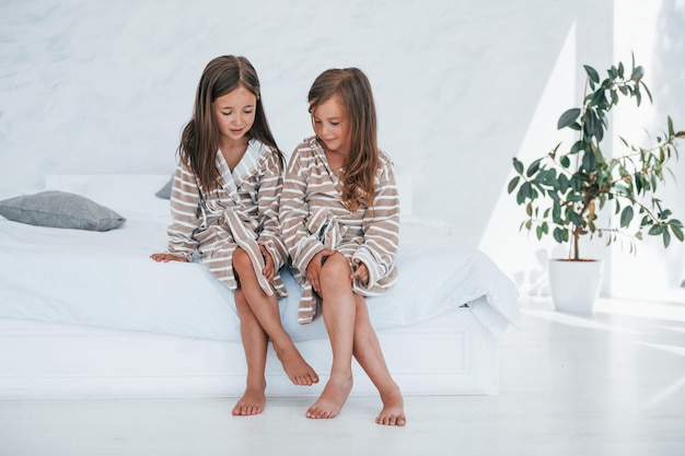 Sitzen auf dem Bett Zwei süße kleine Mädchen drinnen zu Hause zusammen