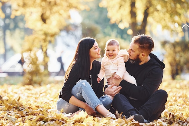 Sitzen auf dem Boden. Fröhliche Familie, die zusammen mit ihrem Kind im schönen Herbstpark Spaß hat.