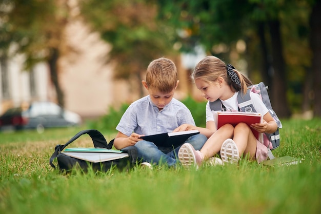 Sitzen auf dem grünen Gras Junge Schulkinder von Jungen und Mädchen sind zusammen im Freien