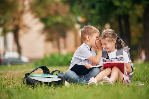 Sitzen auf dem grünen Gras Junge Schulkinder von Jungen und Mädchen sind zusammen im Freien