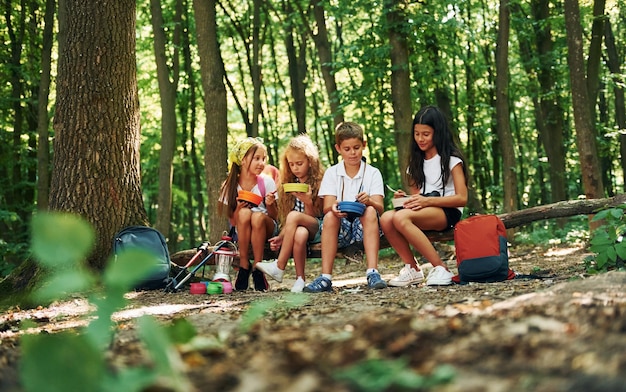 Sitzen und Ausruhen Kinder, die mit Reiseausrüstung im Wald spazieren gehen