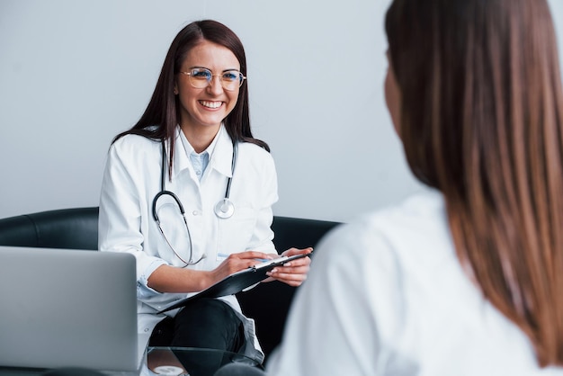 Sitzen und reden Junge Frau besucht eine Ärztin in einer modernen Klinik