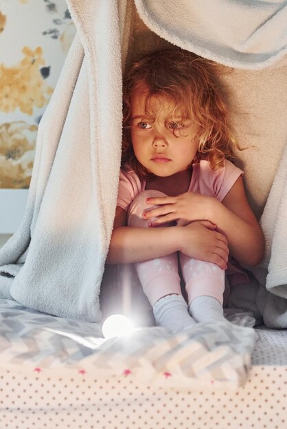 Sitzen unter der Decke Süßes kleines Mädchen in Freizeitkleidung ist tagsüber zu Hause