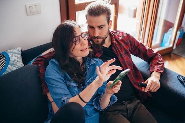 Sitzende Couch der jungen Paare zu Hause Innen, Smartphone betrachtend